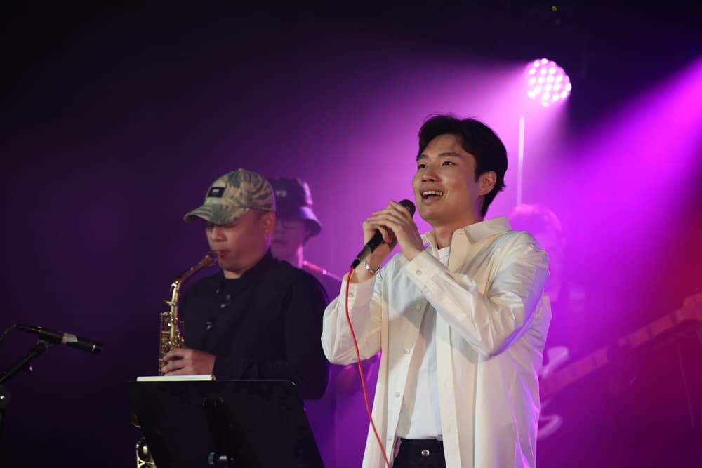 Saxophonist and vocalist performing together under a magenta light wash
